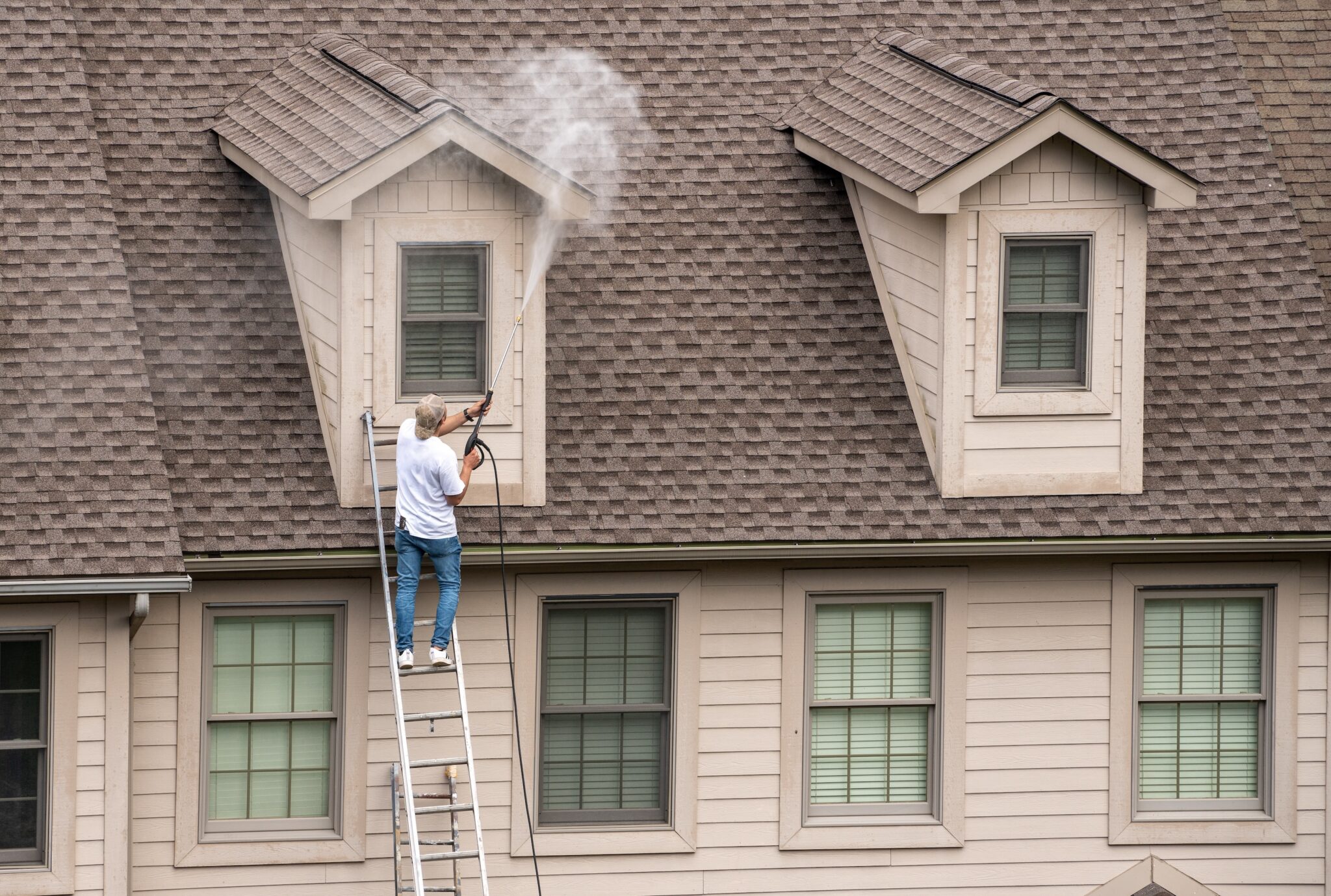 Worker on ladder pressure washing home prior to painting